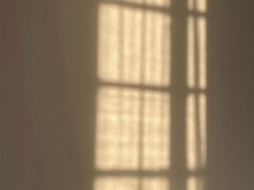 Luz do sol desenhando o contorno de uma janela sobre uma parede clara.